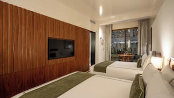 Camera d'albergo con due letti, una TV a schermo piatto montata su un pannello di legno, un tavolino con una lampada e vista sulla città attraverso una finestra.
