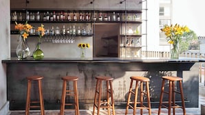 A bar area with wooden stools, a bar counter, and shelves with bottles and glasses. - Hotel Dama (Mexico City)