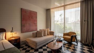 A hotel room with a checkered floor, a sofa, a chair, a coffee table, a lamp, a bed, and a large window with curtains.