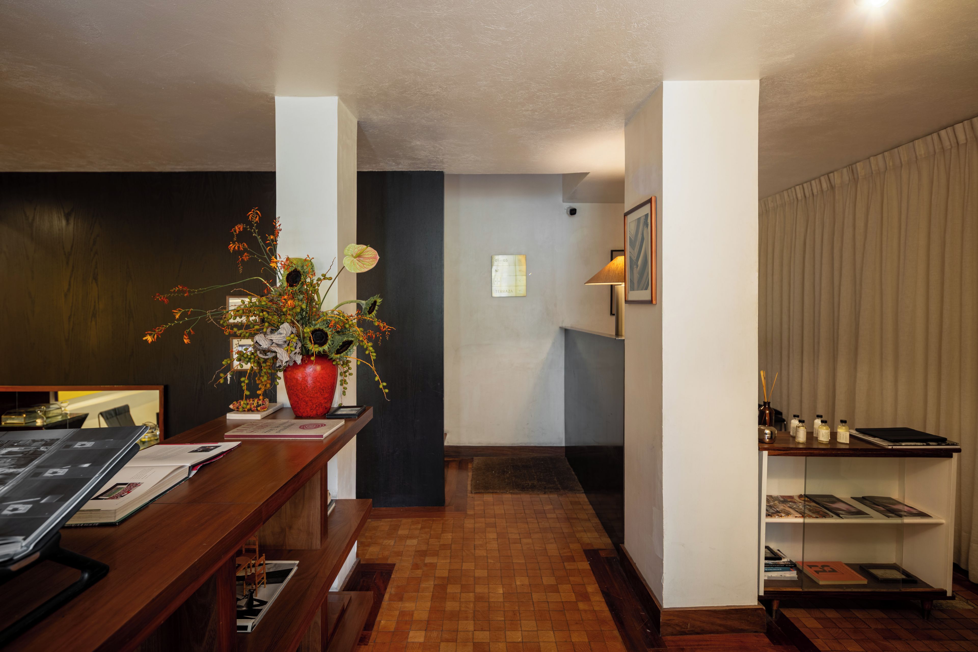 A hotel lobby with a reception desk, a large potted plant, a wall-mounted map, and a bookshelf with magazines.