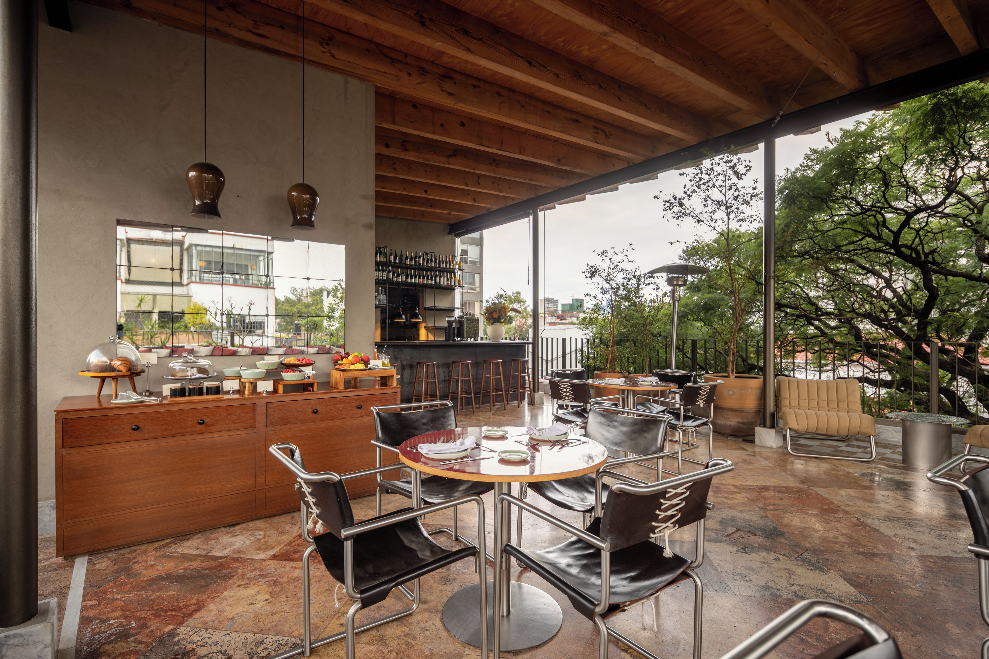 A modern dining area with a bar, wooden ceiling, and large windows overlooking a garden.