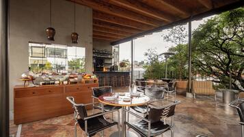 A modern dining area with a bar, wooden ceiling, and large windows overlooking a garden.