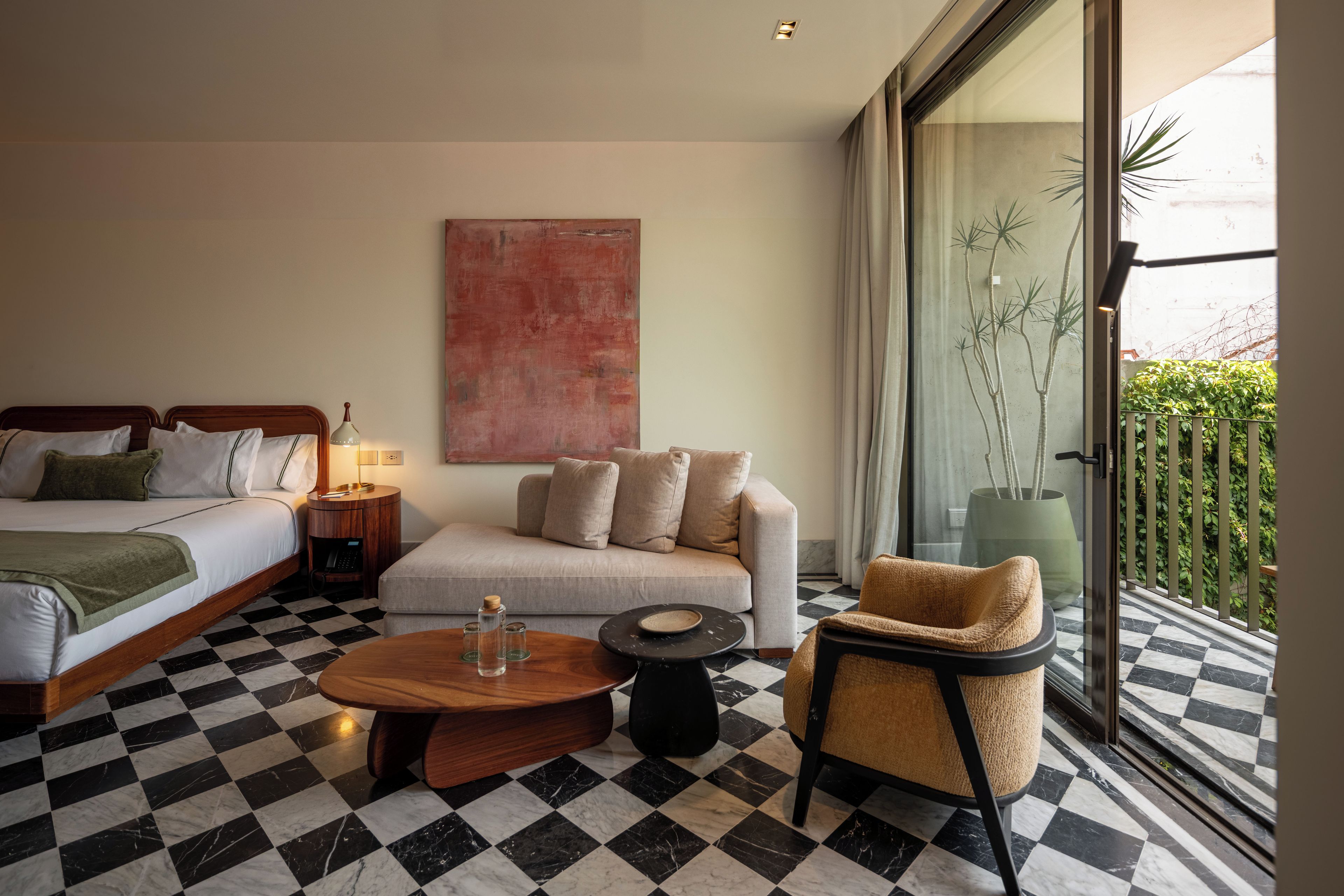 A hotel room with a bed, sofa, armchair, and a checkered floor.