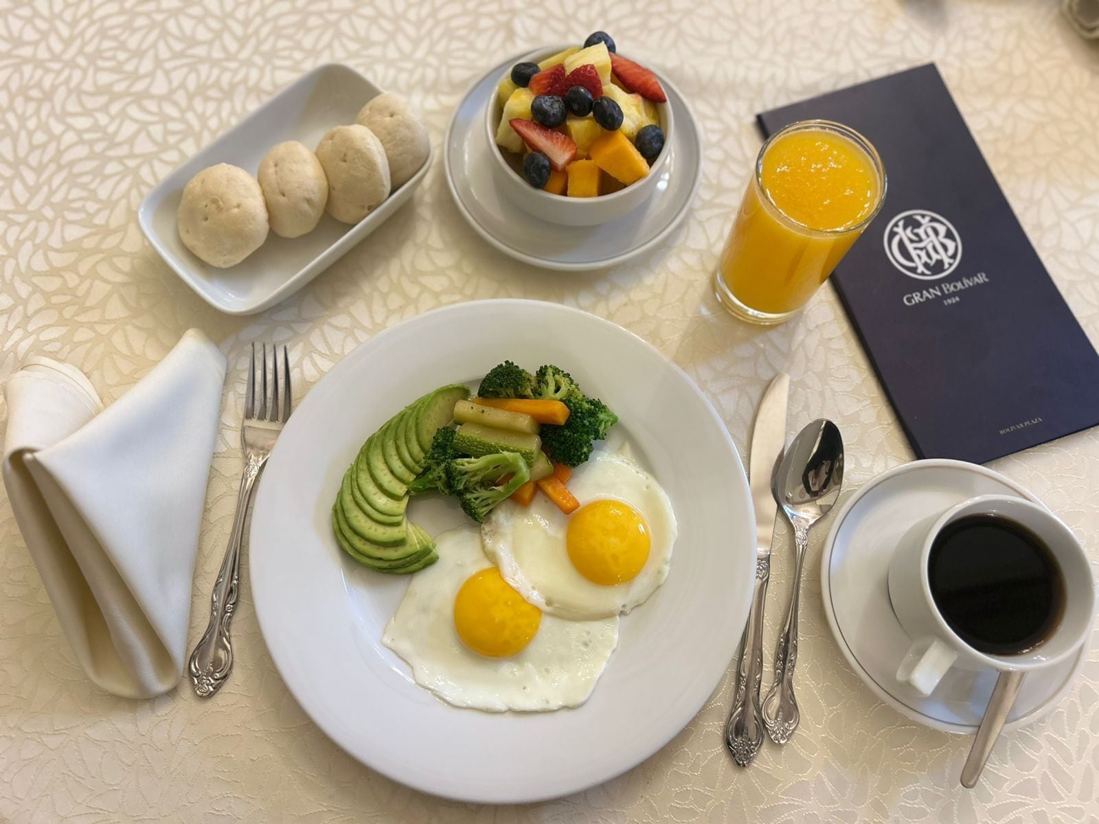 Un plato de desayuno con huevos, verduras y un bol de fruta.