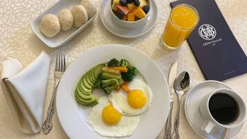Un plato de desayuno con huevos, verduras y un bol de fruta.