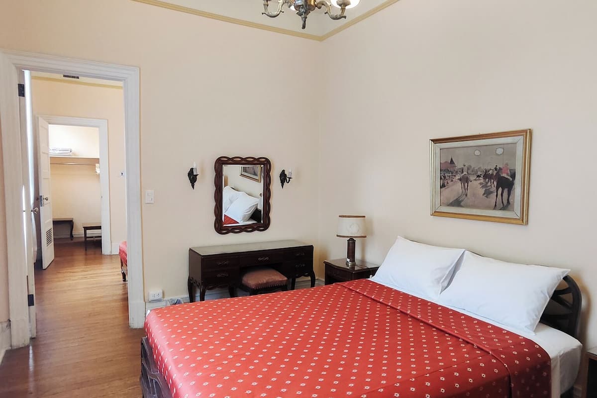 Un dormitorio con cama, cómoda, mesita de noche, espejo, araña y un cuadro en la pared.