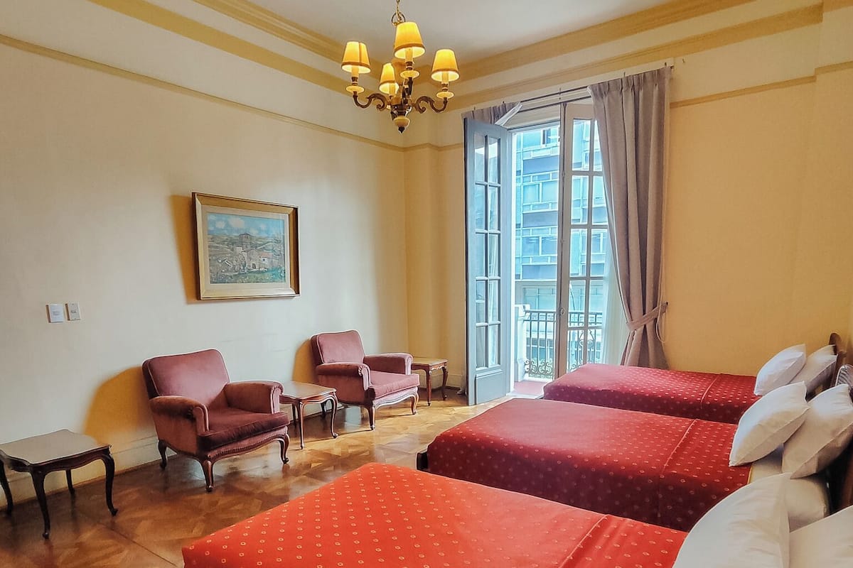 Habitación de hotel con dos camas, un candelabro, un cuadro y una ventana con cortinas.