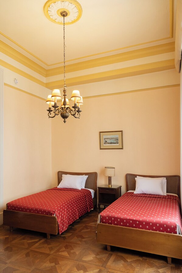 A room with two wooden beds, a chandelier, a framed picture on the wall, and a nightstand with a lamp. - GRAN HOTEL BOLIVAR (Lima)