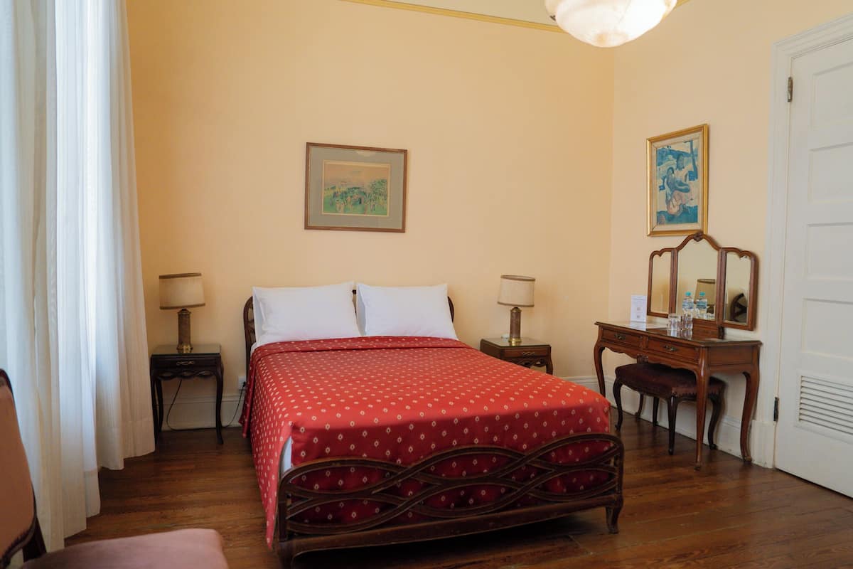 Un dormitorio con una cama, dos mesitas de noche, un aparador, una silla y una puerta.