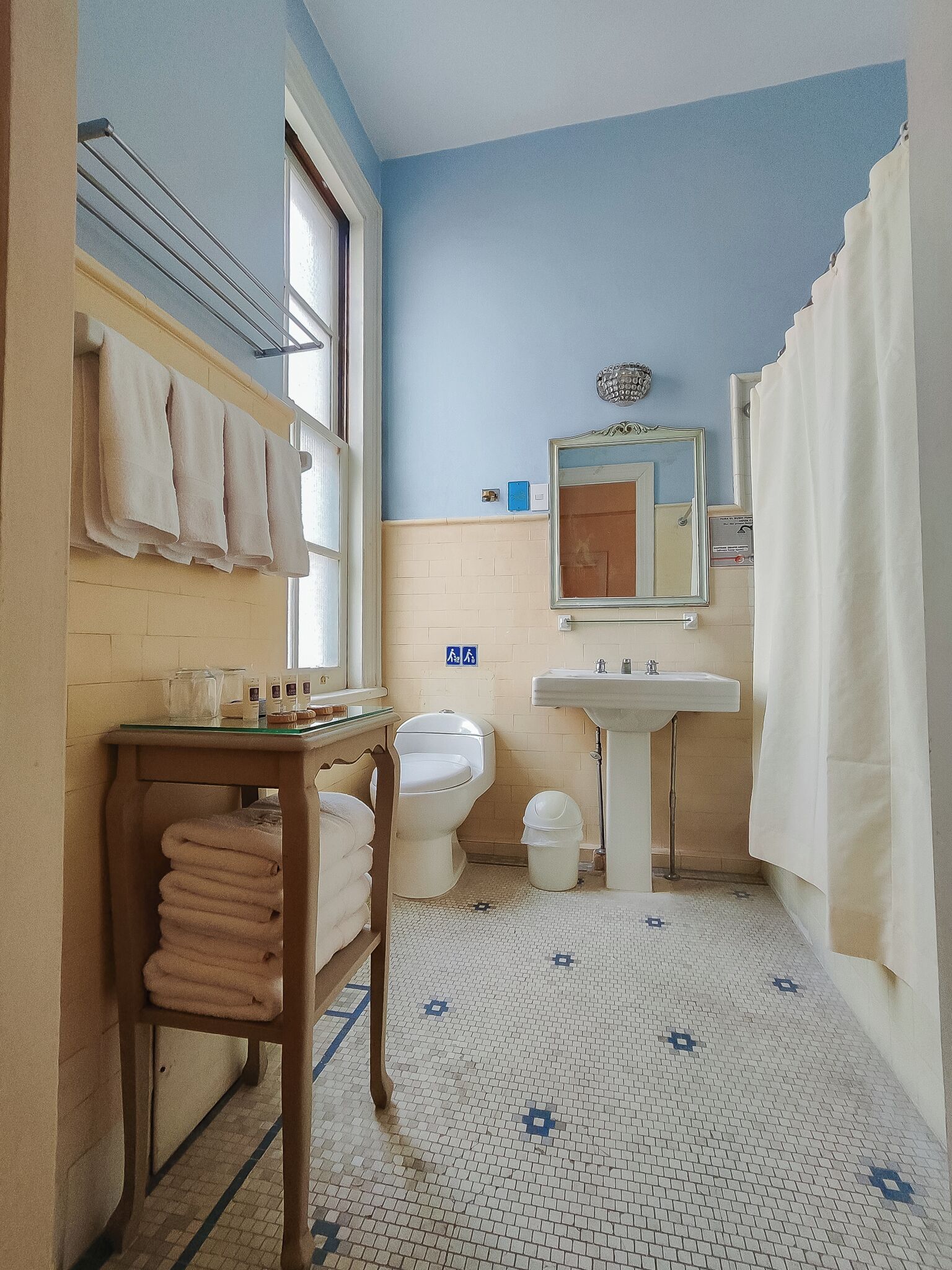 A bathroom with a toilet, sink, and mirror. There are towels on a rack and a window with a view.
