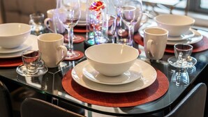 A dining table set with white bowls, cups, and glasses, surrounded by red placemats and a decorative glass centerpiece. - Aspire City Centre Suite - PingPong & Netflix (West Midlands)