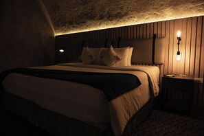 Un dormitorio tenuemente iluminado con una cama grande, cabecera de madera y dos lámparas fijadas a la pared.