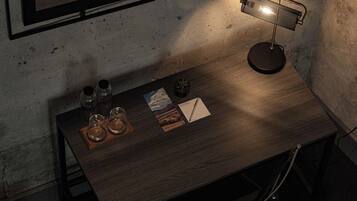 A small, dimly lit room with a wooden desk, a single desk lamp, a mirror, and a small table with a few items on it.