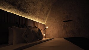 Una habitación acogedora, con poca luz, que tiene una cama, almohadas y una lámpara fijada a la pared.