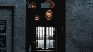 Una habitación tenuemente iluminada, con una pared de piedra rústica, un banco de madera y un ventanal con entramado.