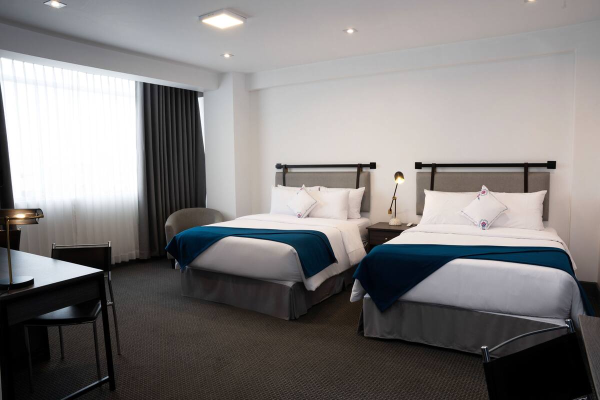 Habitació d'hotel amb dos llits, un escriptori i una cadira.
