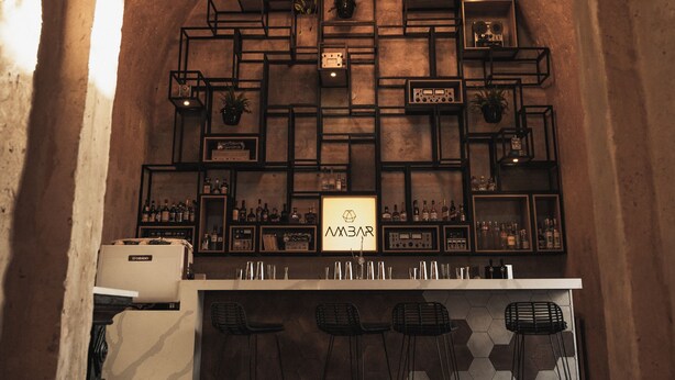 Un área de bar con techo de madera, baldosas hexagonales en la pared y plantas colgantes.