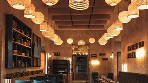 Interior de restaurante con lámparas de mimbre colgantes, suelo de madera y sillas tapizadas en azul.