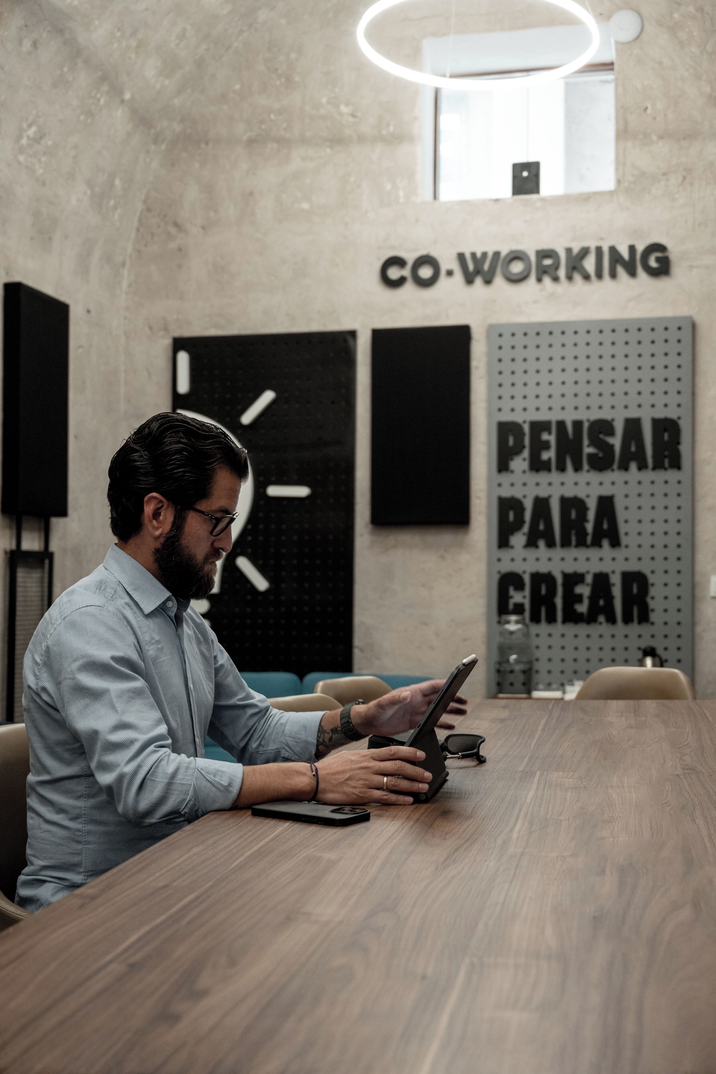 Un hombre sentado a una mesa de madera en una oficina moderna, con un reloj y decoración inspiradora en la pared.