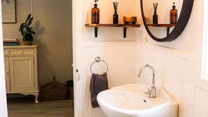 Une salle de bain avec un lavabo blanc, un miroir et des étagères contenant des articles de toilette.