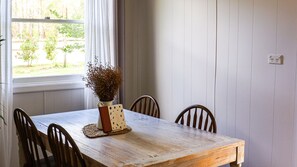 Une table à manger avec quatre chaises en bois, un vase contenant des fleurs séchées et une fenêtre ornée de rideaux blancs.