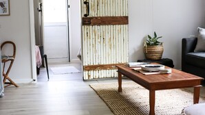 A living room with a wooden coffee table, a woven rug, a wicker basket with a plant, a black sofa, and a wooden chair.