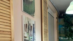 Una habitación con paredes de listones de madera, tres cuadros enmarcados que representan diferentes escenas, una planta en maceta y una silla amarilla.