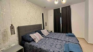 Un dormitorio con una cama grande, una mesita de noche, una lámpara colgante y una ventana con cortinas.