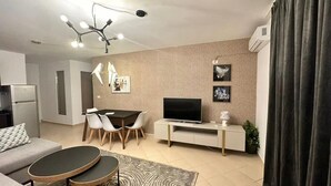 Una sala de estar moderna con un sofá, una mesa de comedor, sillas, un televisor y un tapete estampado.