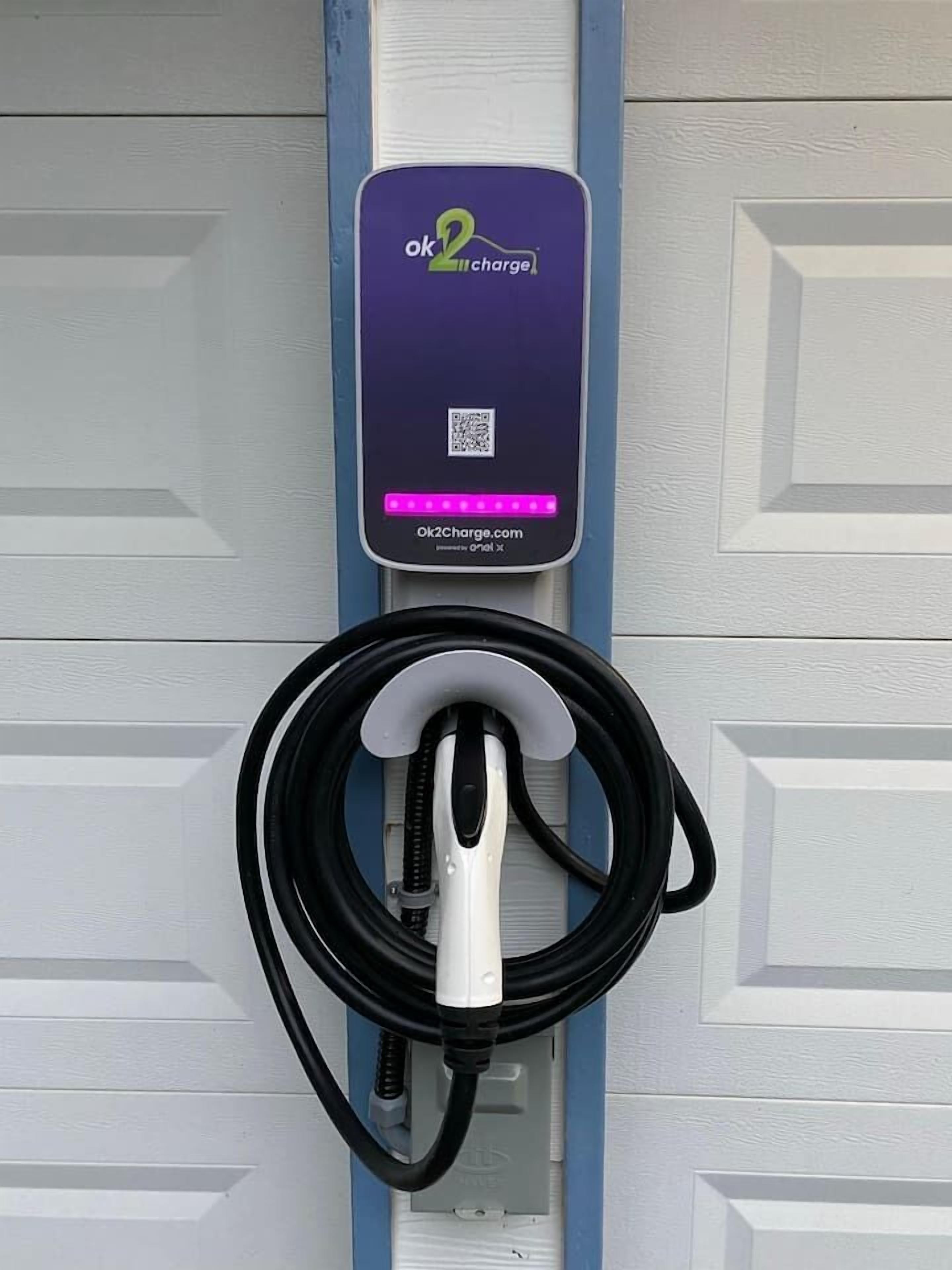 Eine Ladestation für Elektrofahrzeuge mit einer violett-weißen Ladeeinheit und einem schwarzen, aufgewickelten Ladekabel.