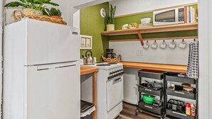 A compact kitchen with a white refrigerator, a stove, a microwave, and a small shelf with kitchenware. - Waterfront Getaway w/ Sauna and BBQ (Longview)