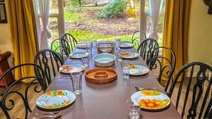 Een eettafel voor zes personen met stoelen, een uitzicht op groen buiten het raam en een gordijn.