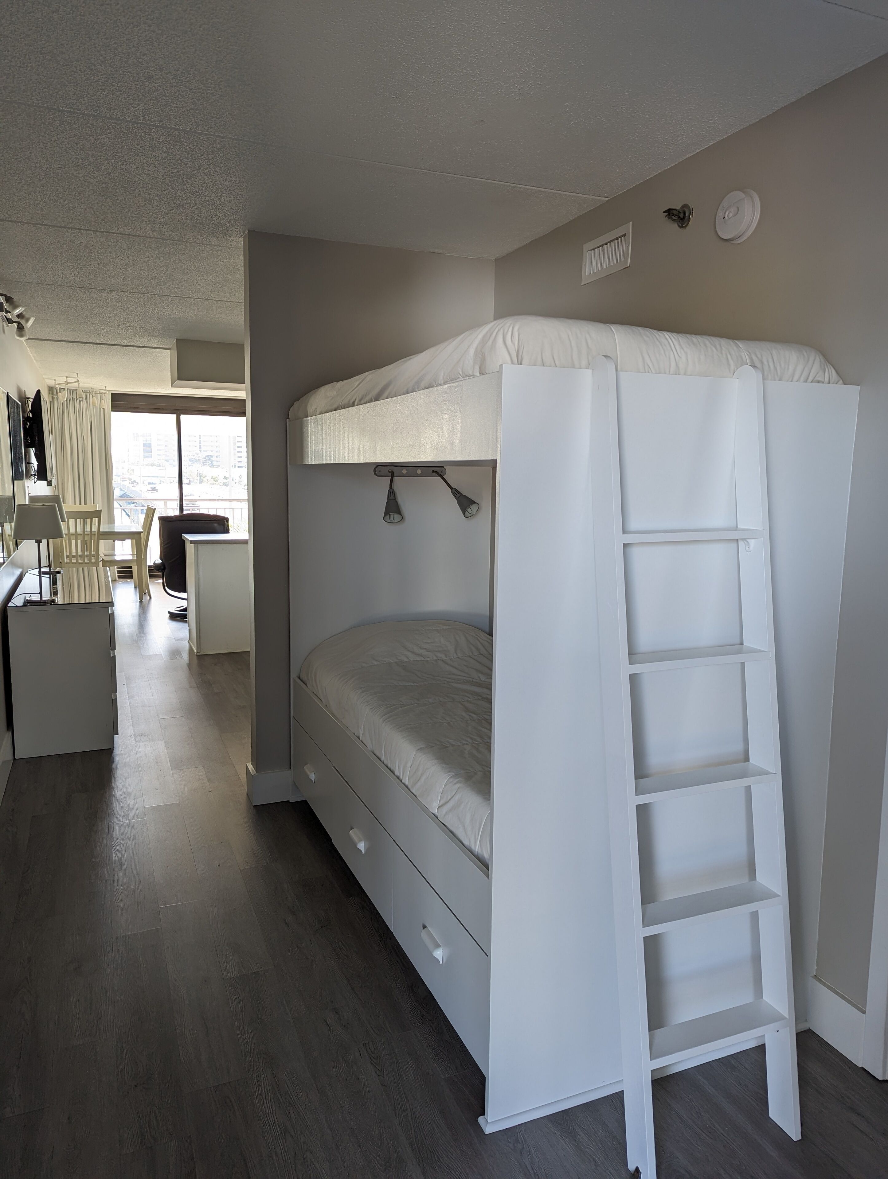 A bunk bed with a ladder, a desk, and a chair in a room with a view of the city.