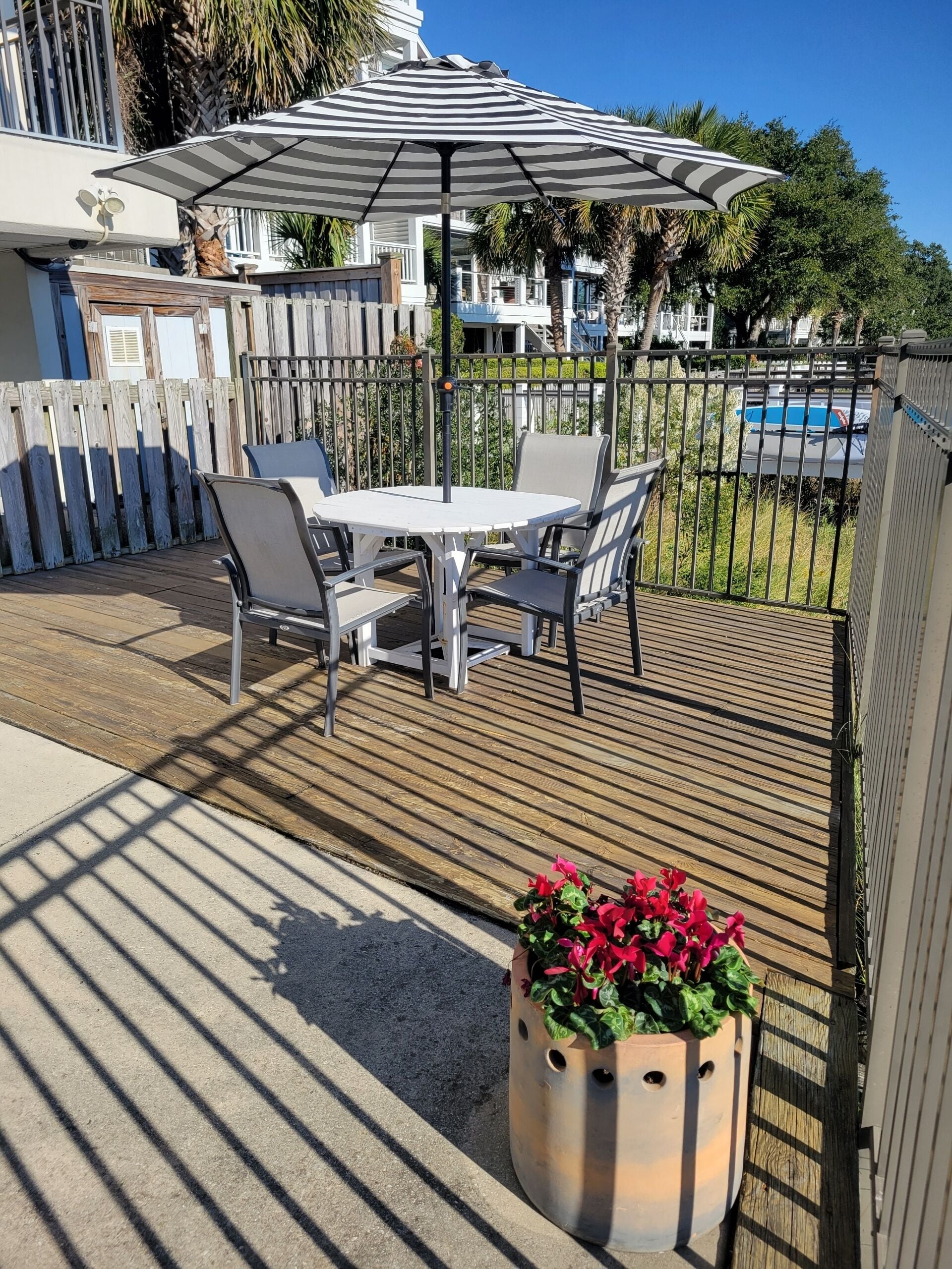 Une terrasse extérieure avec une table et des chaises blanches, un parasol à rayures et un pot de fleurs.
