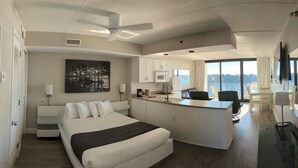 A modern hotel room with a large bed, a kitchenette, a dining area, and a city view. - Harbor Inn (Wrightsville Beach)