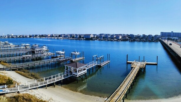 A marina with docks and boats, a clear sky, and a residential area in the background. - Harbor Inn (Wrightsville Beach)