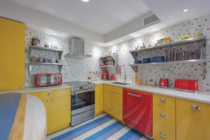 A kitchen with yellow and red cabinets, a stainless steel oven, a red toaster, and a microwave. - Sea Cabins 4C - Beach! Pool! Free Beach Service! (Miramar Beach)