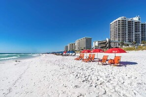 A beach with white sand, red umbrellas, and a large hotel in the background.