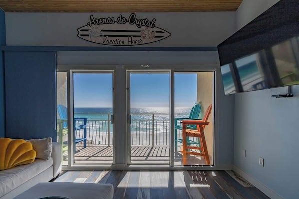 A room with a balcony overlooking the beach, a sign reading "Aronas de Crystal Vacation Home", and a TV mounted on the wall.