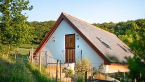 A white building with a sloped roof, a wooden door, and a small balcony with a metal railing. - The Roost in the Blackdowns (Hemyock)
