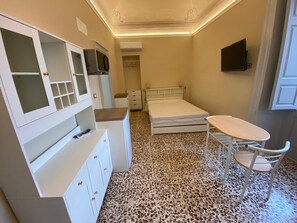 Habitació petita i funcional amb un llit, un escriptori, una cadira i un televisor fixat a la paret.