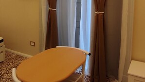A room with a small table and chair, a television mounted on the wall, and a window with brown curtains. - Studio apartment on Plebiscito Street with kitchenette and balcony on the courtyard (Catania)