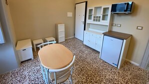 A small, compact room with a kitchenette, a single table, and a TV mounted on the wall. - Studio apartment on Plebiscito Street with kitchenette and balcony on the courtyard (Catania)