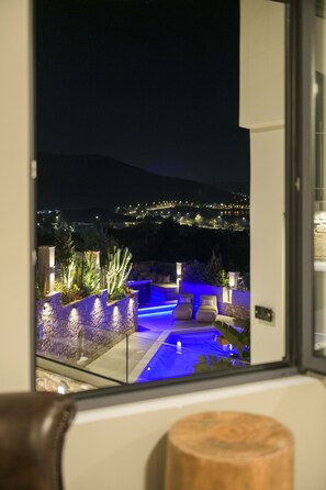 Vista nocturna desde un balcón con piscina, muros de piedra y plantas.