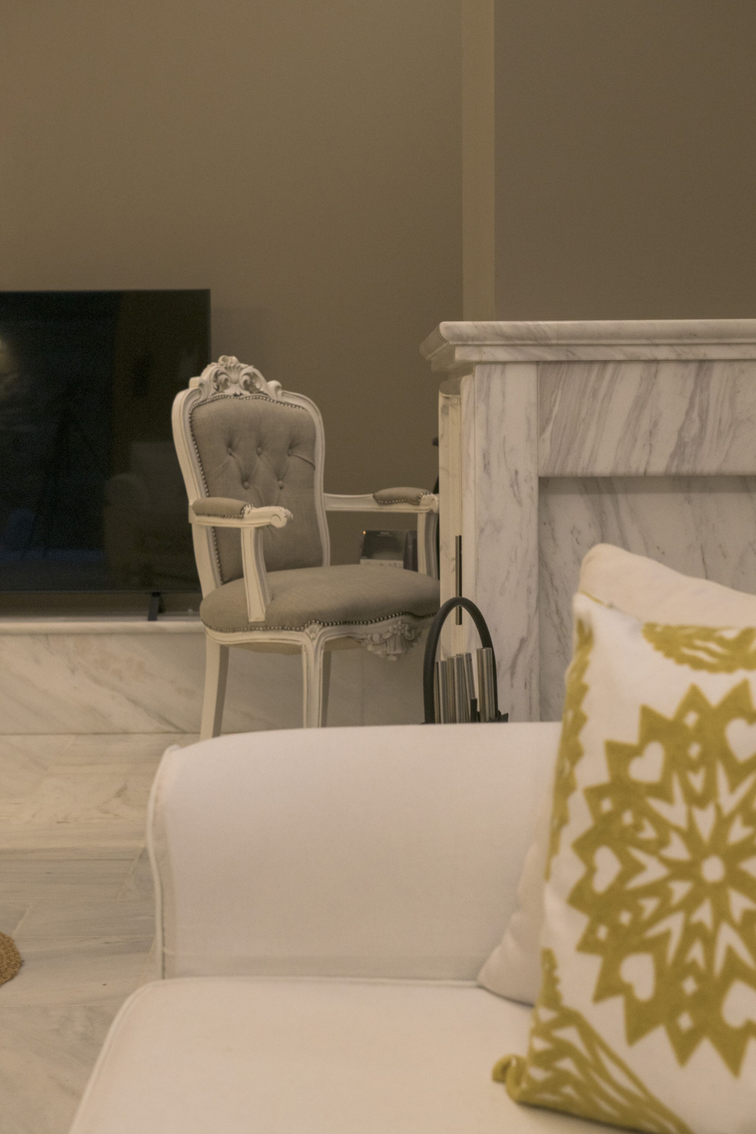 Una sala de estar moderna con un sofá blanco, un sillón capitoné, una chimenea de mármol y un televisor en la pared.