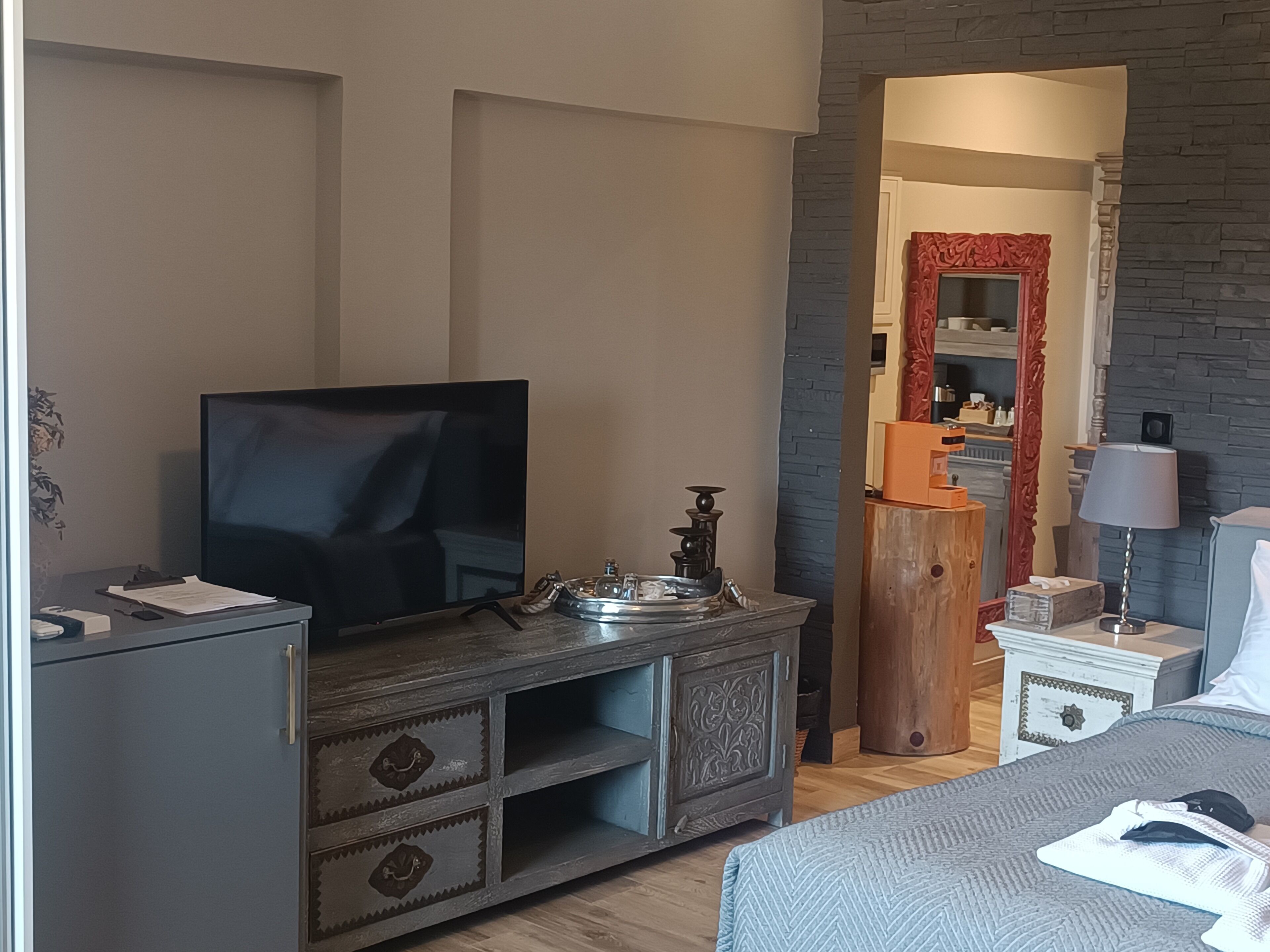 Un dormitorio con cama, televisor, cómoda, mesita de noche y espejo.