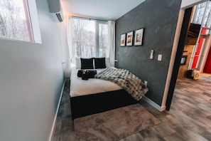 Une chambre moderne avec un grand lit, une fenêtre donnant sur la verdure et un mur foncé orné de tableaux.