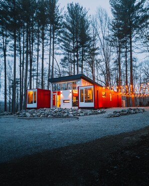 A modern, two-story cabin with large windows and a red exterior, surrounded by a forest.