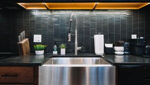 A modern kitchen with dark cabinetry, a stainless steel sink, and a black tiled backsplash. - The Buckeye Box - The James (McArthur)