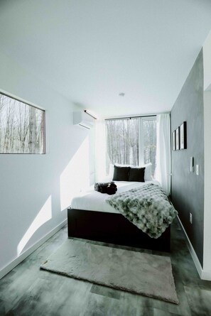A modern bedroom with a large bed, a window with curtains, and a view of trees outside.